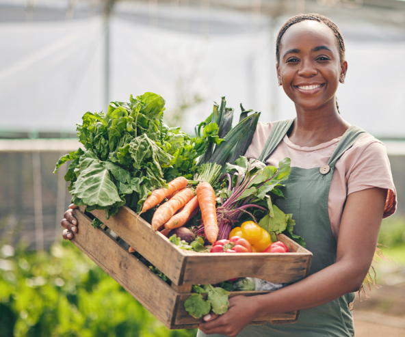 A woman holding a crate of vegetables that includes lettuce, carrots, and peppers. 